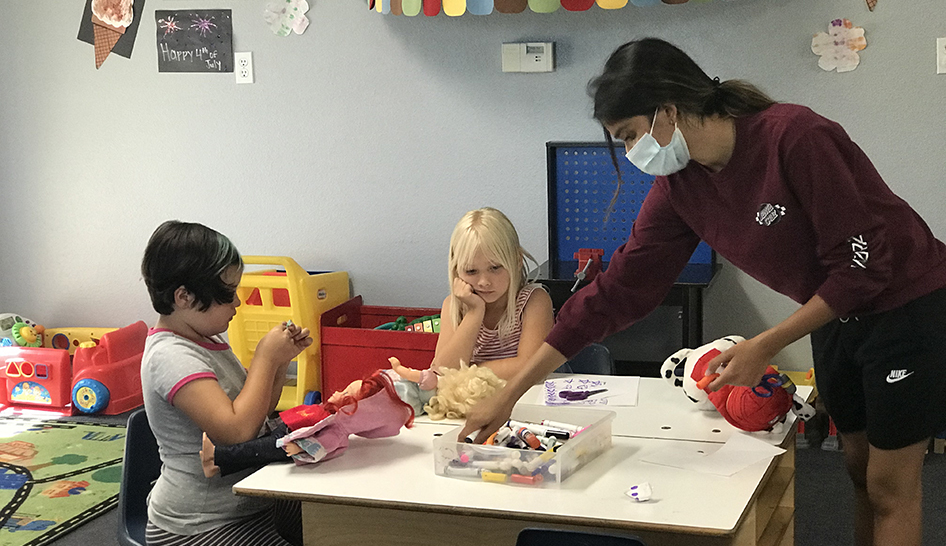 Coronavirus YCRC worker with mask children at desk column